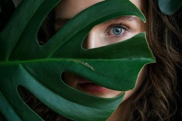 frau-mit-blatt-vor-dem-gesicht-gruen-natur-schoenheit-blaue-augen