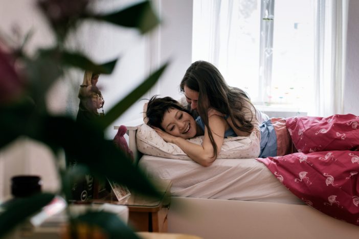 Happy lesbian couple making love in bedroom. Cheerful woman is lying with partner on bed. Multi-ethnic homosexual females are spending quality time at home.